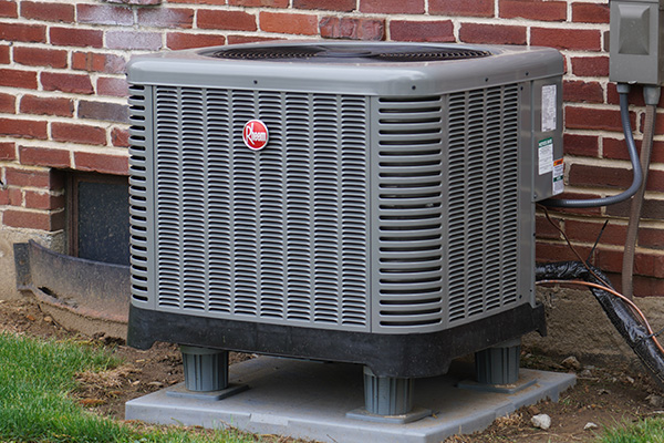Rheem central air conditioning condenser installed beside a brick home